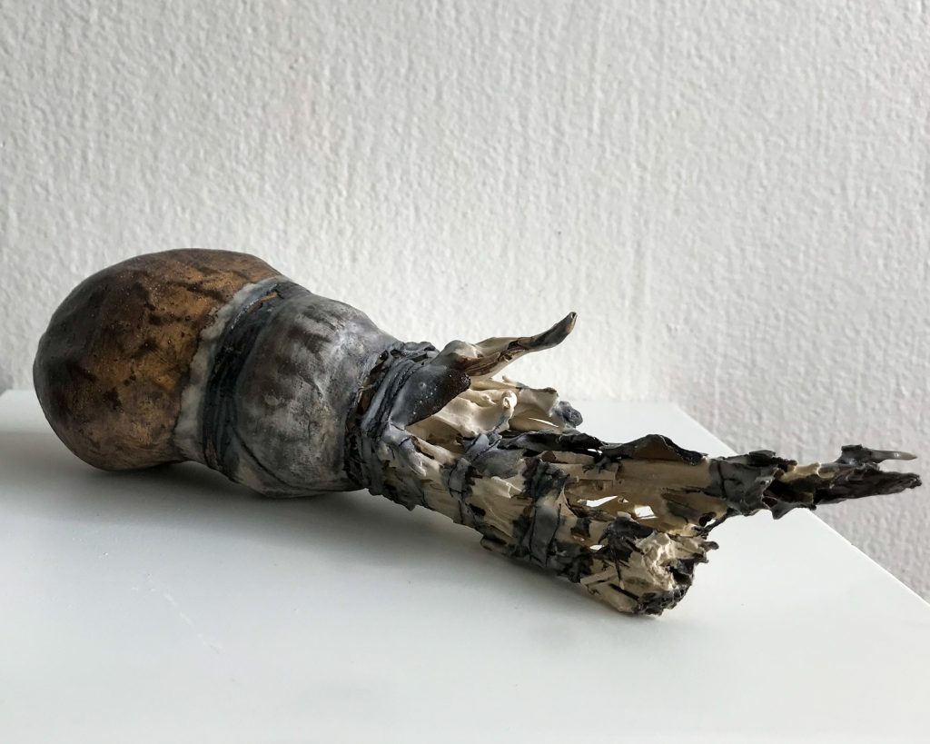 Ceramic sculpture with a smooth brown bulbous end transitioning to jagged, fragmented shards of grey and black.