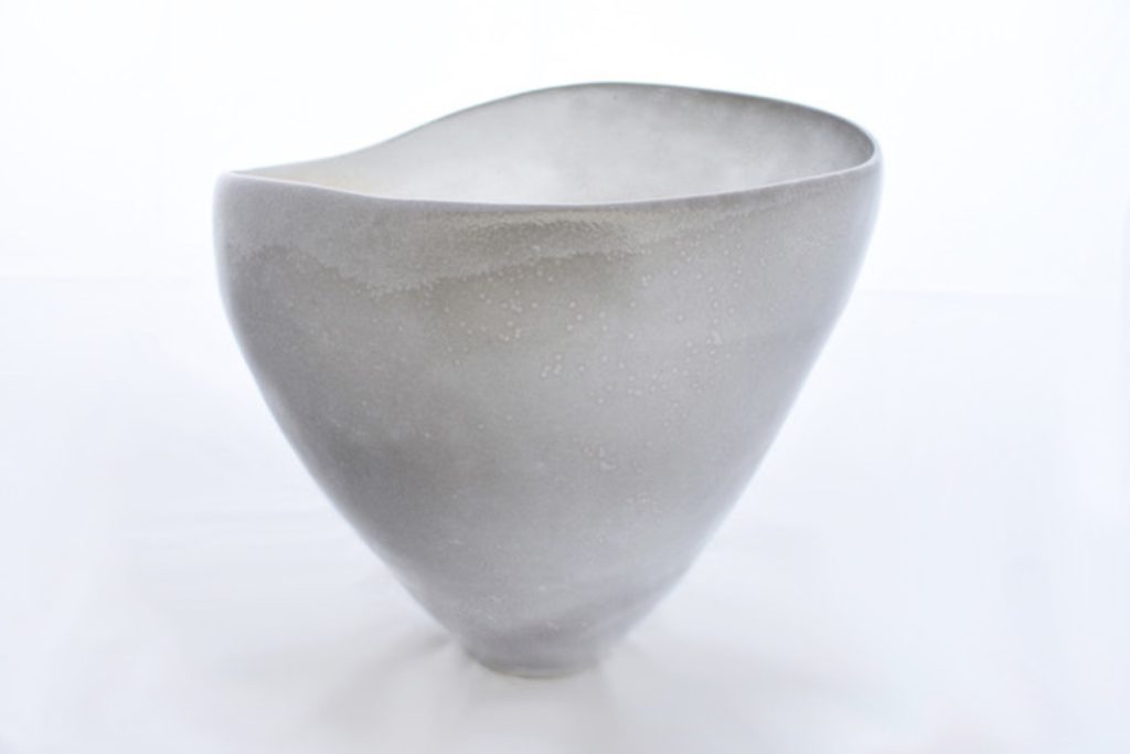 Ceramic sculpture of an asymmetric white porcelain bowl with a gently undulating rim against a white background.