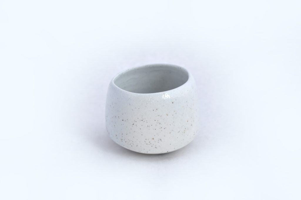 Small round ceramic cup in speckled white glaze with a wide open rim, photographed against a white background.