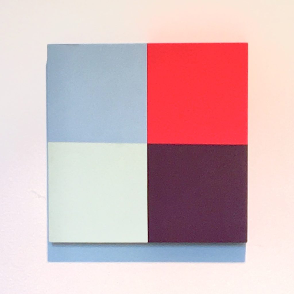 Abstract painting of four flat color quadrants — steel blue, red, pale celadon, and deep purple — on a square panel.