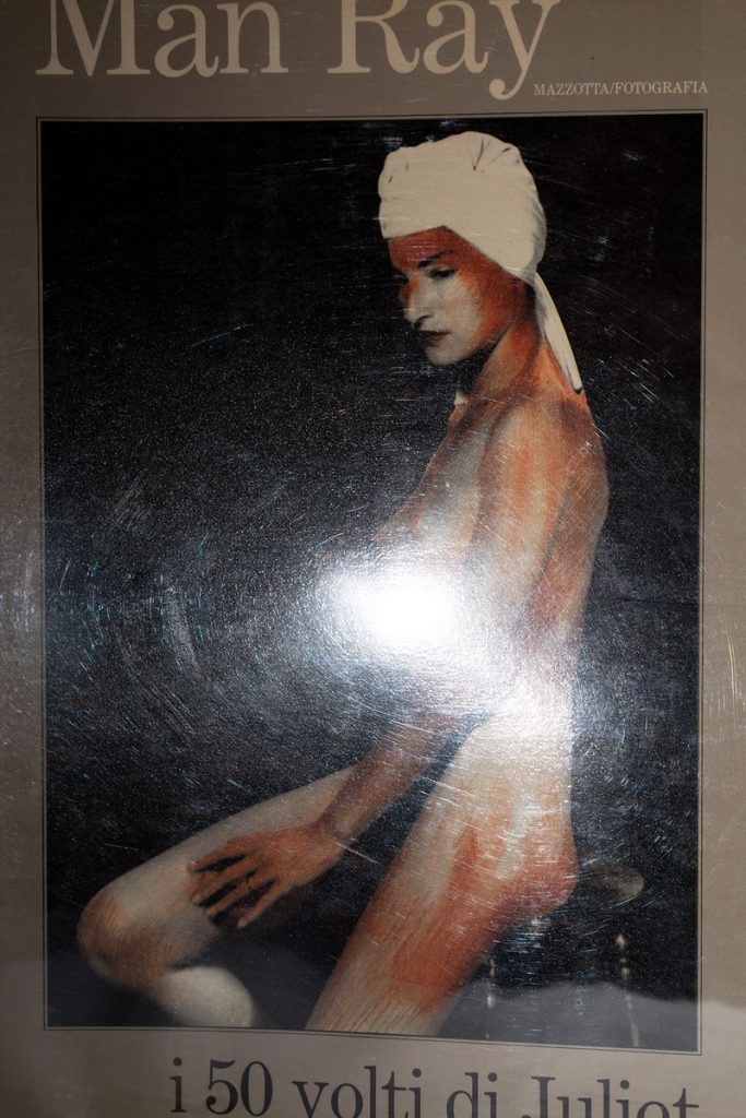 Archival pigment print of a seated nude figure in a white turban against a dark background with warm reddish tones.
