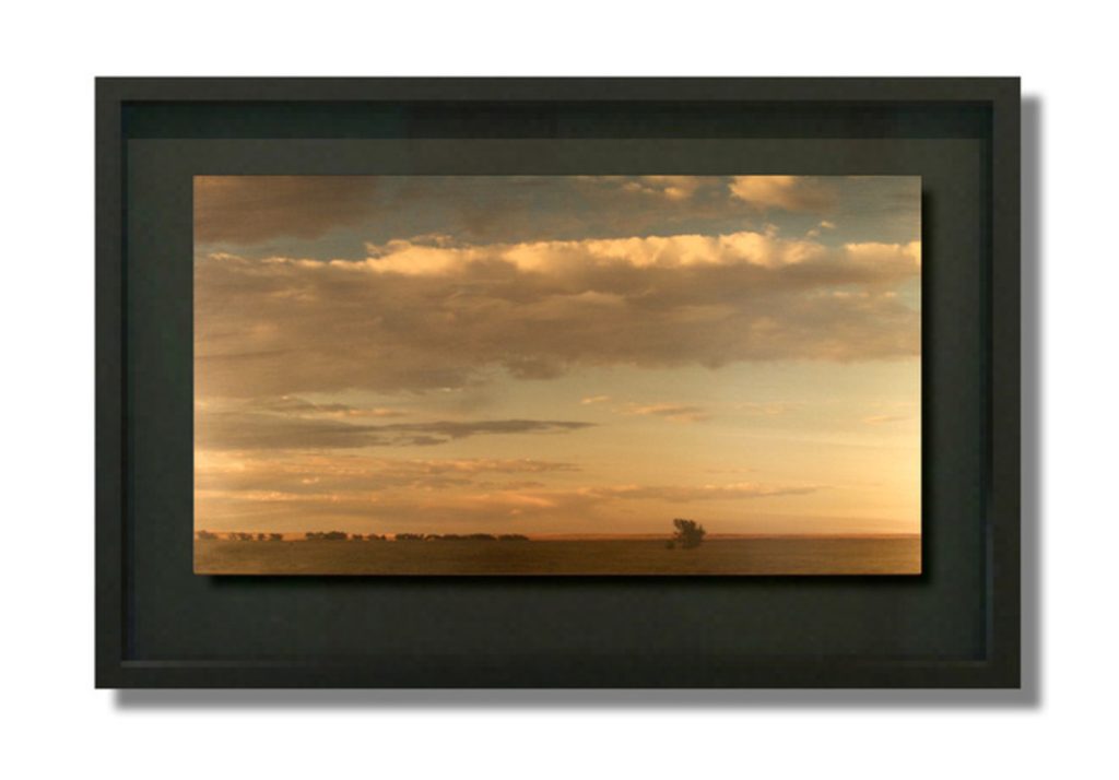 Photograph of a flat prairie landscape at golden hour with a low horizon and a large, cloud-filled sky.