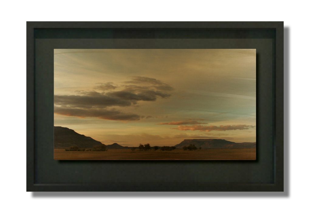 Photograph on painted steel of a wide desert landscape at dusk with mesas, scrub brush, and dramatic cloud-filled sky.