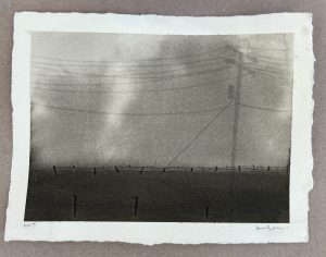 Ink-and-salt print of a utility pole with power lines above a barbed-wire fence in a foggy rural landscape.