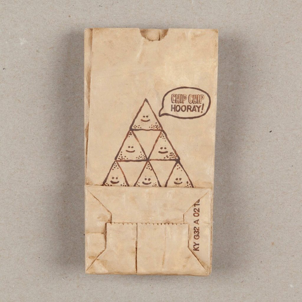 Acrylic painting on wood of a paper bag decorated with smiling cartoon tortilla chips stacked in a pyramid with a speech bubble.